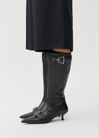 Black leather knee-high boots feature a pointed toe, small kitten heel, and silver buckle accents on the ankle and shaft.