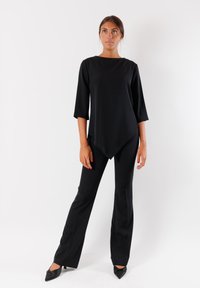 Tunic nera a collo alto con maniche a trequarti abbinata a pantaloni neri su misura. Tessuto liscio, vestibilità affusolata e décolleté a punta.