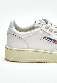 Sneaker in pelle bianca con tomaia testurizzata, punta arrotondata, suola in gomma beige e etichetta con logo laterale impreziosita da un accento bandiera americana.