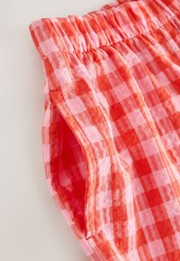 Gros plan sur un short en tissu à motif vichy rouge et rose avec une ceinture élastique et une ouverture de poche latérale.