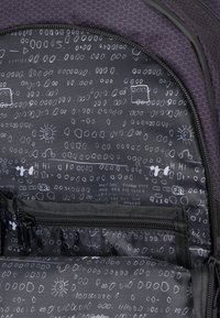 Interno di uno zaino viola con un tessuto testurizzato nero caratterizzato da motivi astratti bianchi, linee e simboli, tra cui il sole e varie forme.