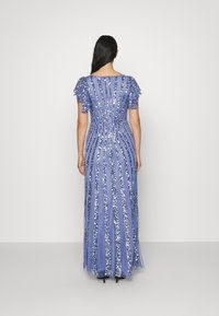 Dlouhé modré šaty s krátkými volánkovými rukávy, zdobené pruhy z flitrů pro texturu a lesk, s přiléhavým pasem a splývavou sukní.