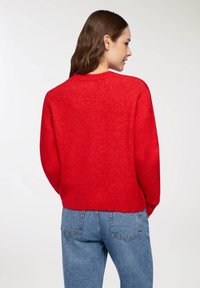 Czerwona dzianinowa sweter z okrągłym dekoltem i ściągaczami, zestawiony z niebieskimi dżinsami o wysokim stanie; gładka tekstura i luźny krój.