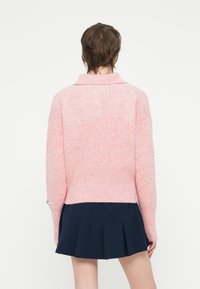Maglione lavorato a maglia rosa chiaro con colletto, texture a coste e spalle scese, abbinato a una gonna plissettata blu navy.