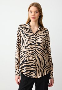 Langarmblouse van zijdezachte stof, met een beige basis en zwarte zebrapatronen. Knopsluiting aan de voorkant, klassieke kraag en afgeronde zoom.