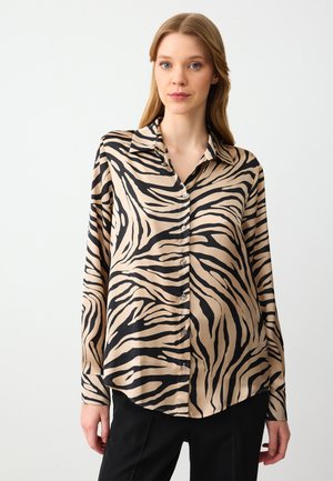 Blusa a maniche lunghe in tessuto setoso, con una base beige e righe zebrate nere. Chiusura con bottoni davanti, colletto classico e orlo curvo.