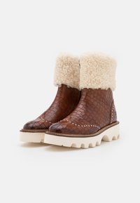 Botas de tobillo de cuero marrón con patrón trenzado, puño blanco esponjoso y suela blanca gruesa. Presenta tachuelas decorativas en la punta.