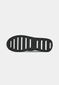 Black shoe sole featuring a textured rubber design with wide grooves, white accents, and branding on the surface.