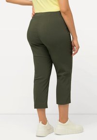 Pantalons cropped vert olive en tissu doux, avec une texture lisse et une taille haute, assortis à des baskets compensées blanches.