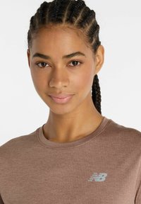 Brown textured athletic shirt with a crew neckline, featuring a reflective New Balance logo on the left chest area.