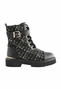Stivaletto nero in tweed con lacci frontali, dettagli in fibbia, suola in gomma e dettagli metallici. Presenta un tessuto testurizzato e elementi in pelle liscia.