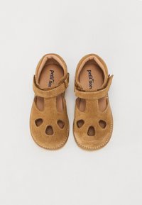 Bruna mockaskor för barn med utskurna mönster och kardborreband. Har en beige innersula och sydda detaljer längs kanterna.