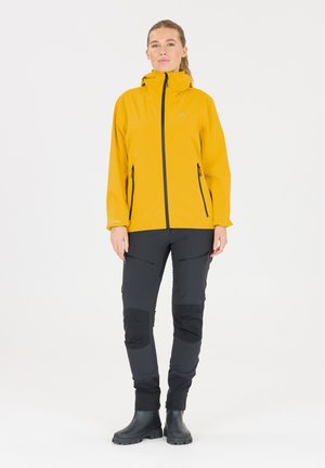 Gul vattentät jacka med svarta dragkedjor, tillsammans med svarta byxor med zip-fickor och knäskydd. Svarta gummistövlar fulländar outfiten.