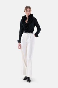 Black blouse with ruffled neckline, white pleated trousers, and black pointed toe heels, featuring a slim black belt.