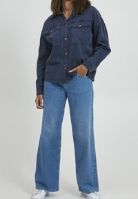 Navy blue shirt with two front pockets and brown buttons; paired with light blue wide-leg jeans and white sneakers. Simple, casual look.