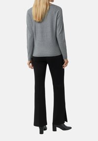 Szary sweter z długim rękawem i okrągłym dekoltem, połączony z czarnymi spodniami dzwonami z bocznymi rozporkami, noszony z czarnymi botkami na obcasie.