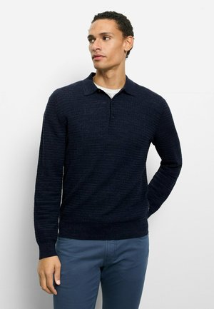 Marineblauer, strukturierter Langarm-Polo-Pullover mit Kragen und drei Knöpfen, kombiniert mit hellblauen Hosen.