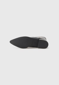 Zapato de vestir negro de punta afilada acostado de lado, mostrando suela de goma con textura antideslizante y tacón bajo, talla 43.
