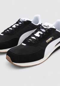 Czarno-białe sneakersy z zamszu i materiału, z białym paskiem, czarnymi sznurówkami i złotym logo na boku.