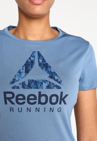 T-shirt da corsa Reebok in azzurro chiaro, con un design a logo testurizzato di colore blu scuro. Il tessuto è liscio con scollatura a girocollo e maniche corte.