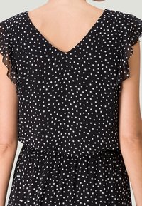 Vestito nero con pois bianchi, scollatura a V e maniche corte con volant. Tessuto leggero con pois bianchi, vita arricciata per una vestibilità comoda.