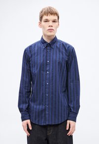 Tumesinine nööpidega särk vertikaalsete mustade triipudega, pikkade varrukatega ja terava kraega. Esiküljel bränditud tikand ja sinised nööbid.