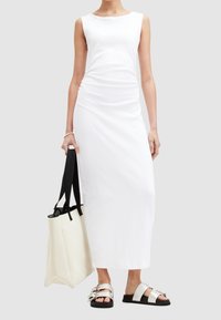 Weißes ärmelloses Kleid mit gerafftem Seitendetail, kombiniert mit einer schwarz-wei ßen Tragetasche und Sandalen mit silbernen Riemen. Glatte Stofftextur.