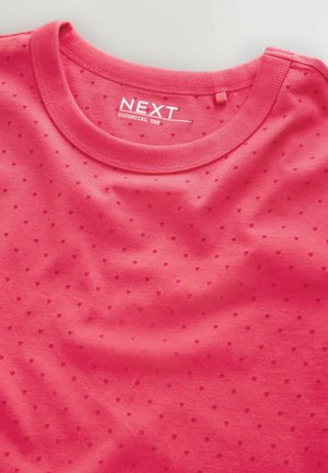 Różowy bawełniany t-shirt z okrągłym dekoltem, wzorem drobnych kropek w kształcie serc oraz metką "NEXT ESSENTIAL TEE" na kołnierzu.