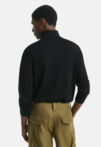 Zwarte pullover trui met een hoge kraag, voorzien van lange mouwen en een gladde textuur, gecombineerd met olijfgroene cargobroeken met achterzakken.