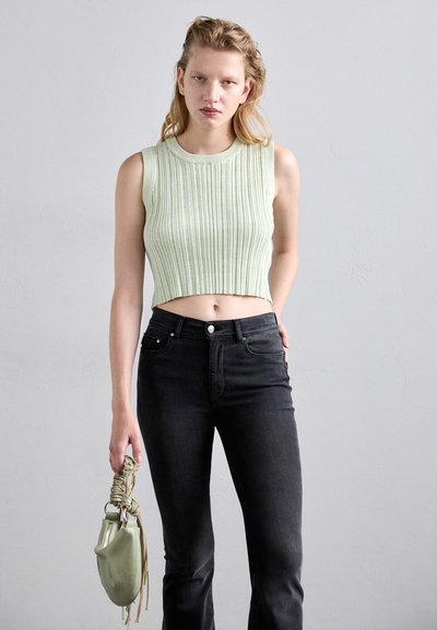 Light green, ribbed crop top with a round neckline paired with dark black fitted jeans. A small, knotted green handbag is held in one hand.