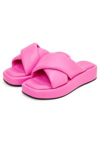 Sandales à semelle plate roses avec un design à brides croisées, en matériau synthétique lisse, semelle épaisse et semelle intérieure rembourrée. Accent de semelle noire.