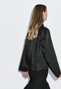 Giacca oversize a righe bianche e nere con una vestibilità rilassata, caratterizzata da un colletto ripiegato e maniche lunghe. Tessuto morbido, design minimale.