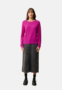 Fuchsia trui met een ronde halslijn en geribbelde manchetten, gecombineerd met een zwarte spijkerrok. De schoenen zijn zwart met een chunky zool.