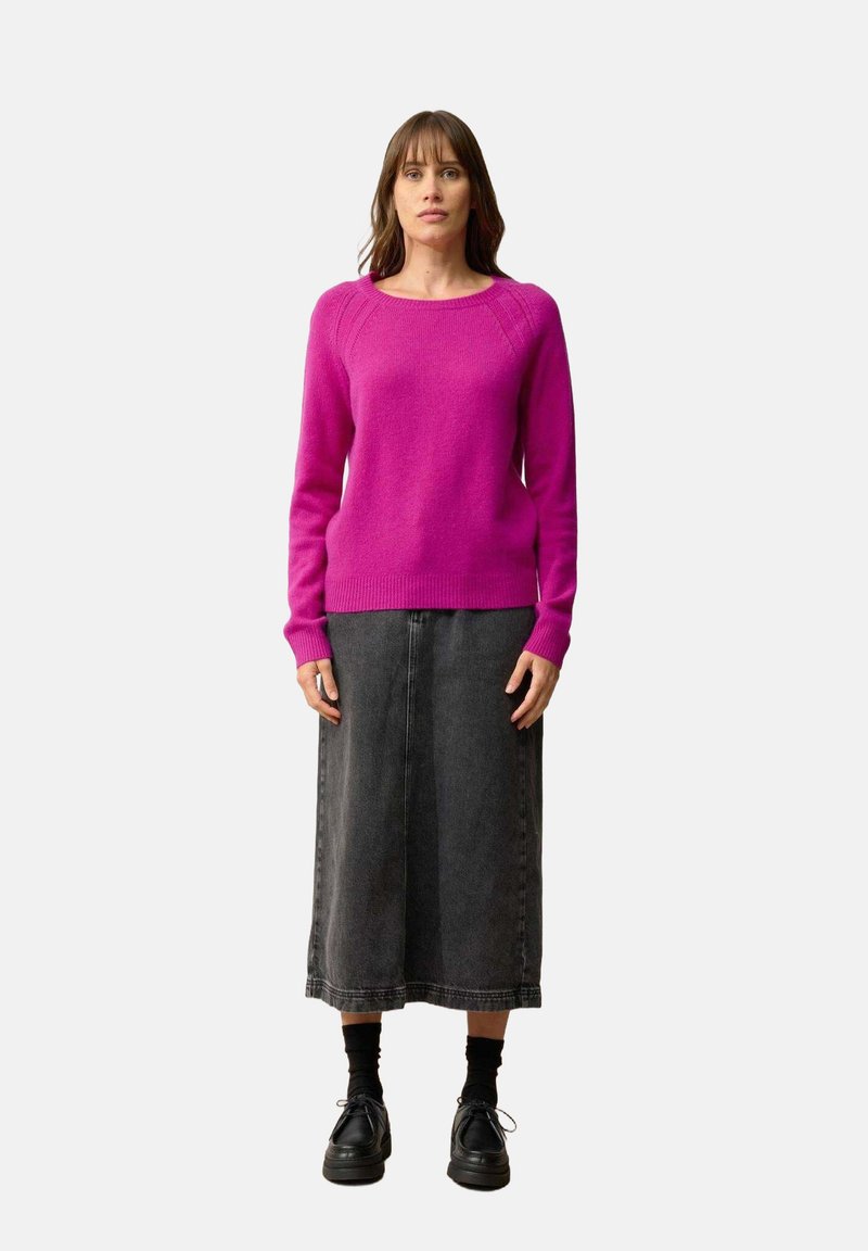 Fuchsia trui met een ronde halslijn en geribbelde manchetten, gecombineerd met een zwarte spijkerrok. De schoenen zijn zwart met een chunky zool.