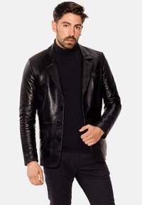 Blazer de cuero negro con un diseño entallado, que cuenta con solapa muesca, tres botones y un bolsillo en el pecho. Textura suave.