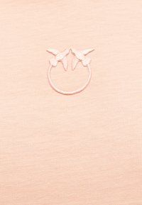 Ανοιχτό ροζ ύφασμα με ένα διακριτικό κεντητό κύκλο που φιλοξενεί δύο πουλιά που κοιτούν το ένα το άλλο στο πάνω κέντρο.