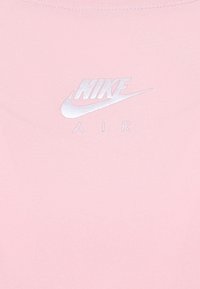 Logo de Nike Air impreso en blanco sobre una tela suave de color rosa, que probablemente forma parte de una prenda de vestir.