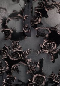 Čierna sieťovina s kvetinovým vzorom, ktorá obsahuje tmavo- a svetloružové motívy. Dizajn zahŕňa gombíkovú légou pri výstrihu.