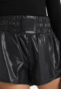 Černé, lesklé nylonové šortky s nařaseným elastickým pasem. Disponují čtvercovou nášivkou s embosovaným nápisem "IVY PARK". Hladký povrch a elegantní design.