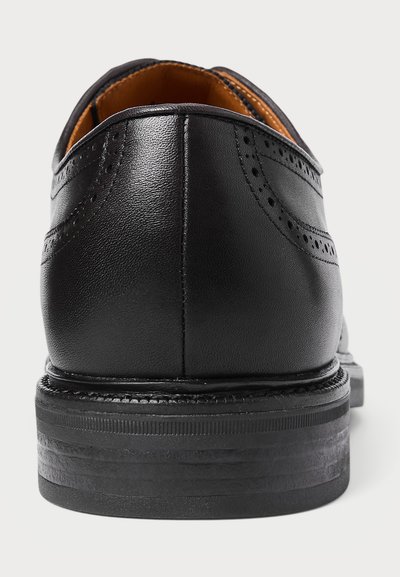 Pantofii eleganți din piele neagră, cu detalii brogue, văzuți din spate, care arată talpa cusută și interiorul căptușit în nuanța chcă.