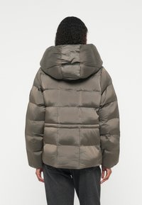 Veste matelassée couleur vert olive avec un design en dégradé, grande capuche et une texture légèrement brillante, dotée de poignets élastiques et d'une coupe décontractée.