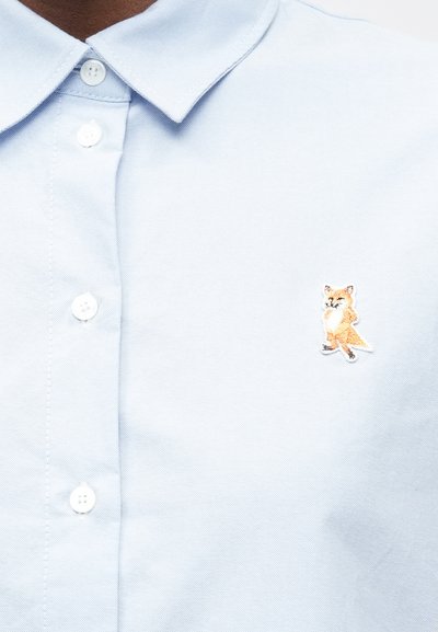 Šviesiai mėlynas medvilninis polo marškinėliai su klasikine apykakle, ant kairiojo krūtinės puikuojasi detaliai išsiuvinėta lapės dizainas.