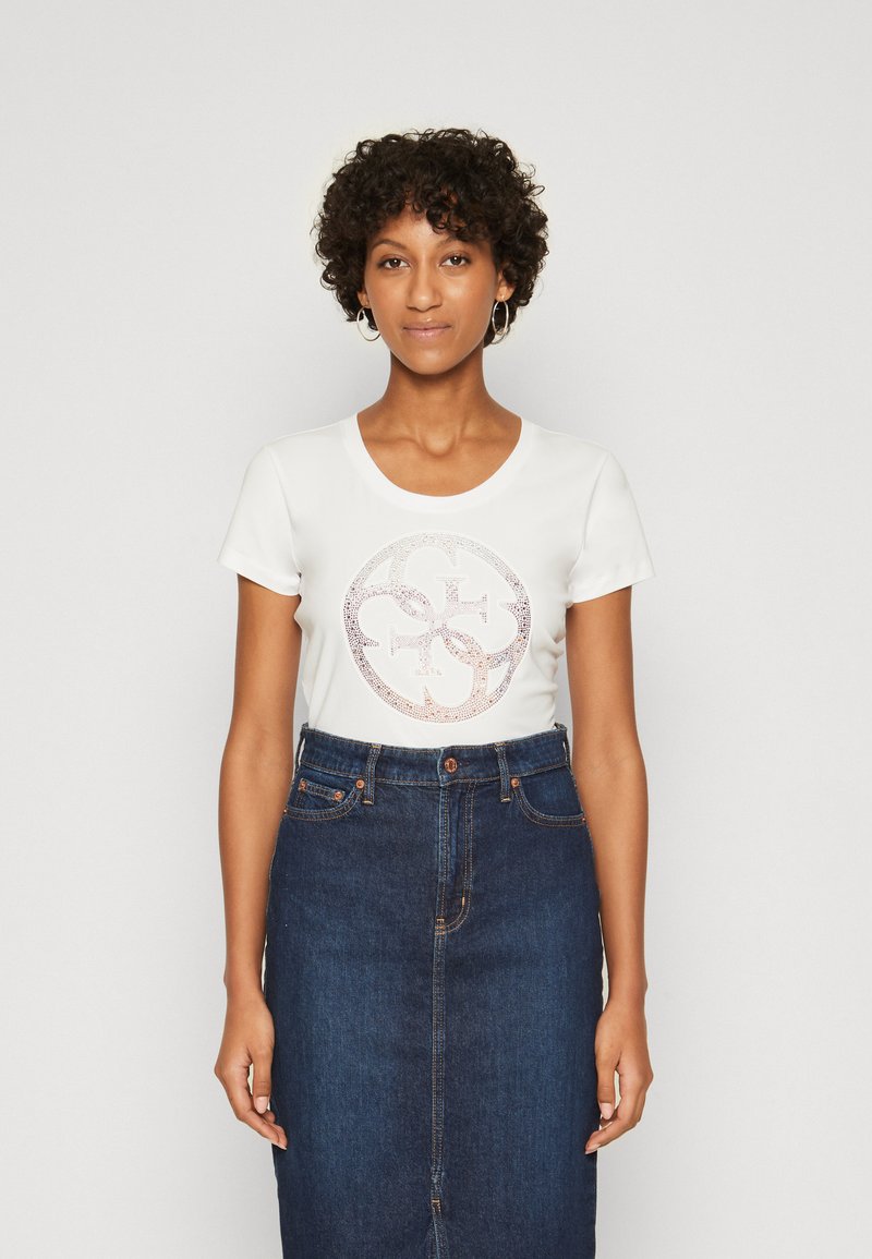 Camiseta blanca de manga corta con un diseño de logo circular de purpurina en el frente, combinada con una falda lápiz de mezclilla de talle alto.