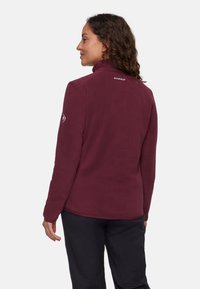 Bordowy polarowy kurtka z wysokim kołnierzem, z logo na plecach i kontrastowym detalem na rękawie. Miękka tekstura i dopasowany krój.