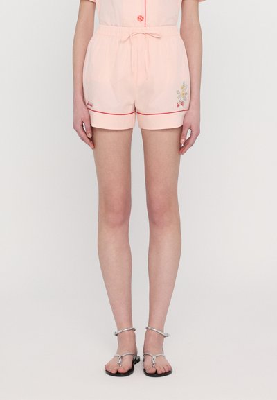 Lys pink shorts med rød kant og elastisk talje, med blomsterbroderi på siden. Sammen med sølvfarvede sandaler med stropper.