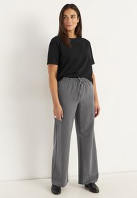 Zwarte t-shirt met korte mouwen, gecombineerd met grijze wijde broek, voorzien van een elastische tailleband en subtiele textuur, afgemaakt met zwarte schoenen.