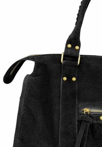 Sac à main en daim noir avec fermeture éclair dorée, clous et boucle de sangle, présentant un gros plan du coin supérieur et de la poignée.