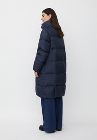 Parka blu navy con colletto alto e maniche lunghe, caratterizzata da una silhouette ampia e sezioni trapuntate. Abbinata a pantaloni di jeans a gamba larga.