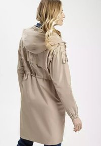 Jasno beżowy parka z kapturem, ze zwężoną talią i elastycznymi mankietami. Posiada boczne kieszenie i luźny krój. Gładki, lekki materiał.
