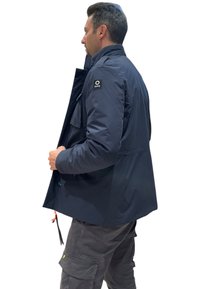 Giacca blu navy dal taglio ampio, con tasca laterale, collo alla coreana e logo sulla spalla sinistra. Realizzata in materiale liscio e leggero.